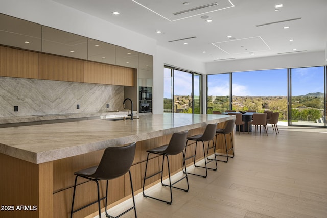 kitchen with a large island, sink, light hardwood / wood-style flooring, tasteful backsplash, and a kitchen bar