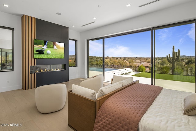 bedroom featuring access to exterior, light wood-type flooring, and a fireplace