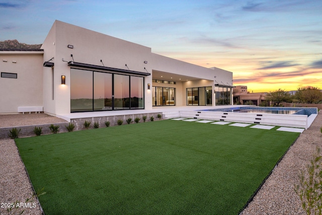 back house at dusk featuring a yard and a patio