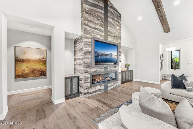 living room featuring high vaulted ceiling, beamed ceiling, light hardwood / wood-style flooring, and a fireplace