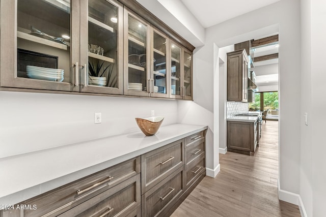 bar with dark brown cabinets, light hardwood / wood-style floors, beamed ceiling, and backsplash