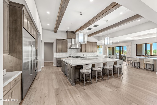 kitchen with light stone counters, beam ceiling, decorative light fixtures, light hardwood / wood-style flooring, and a large island