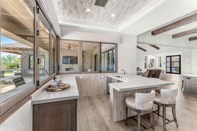 kitchen with a stone fireplace, light wood-type flooring, sink, an island with sink, and a kitchen breakfast bar