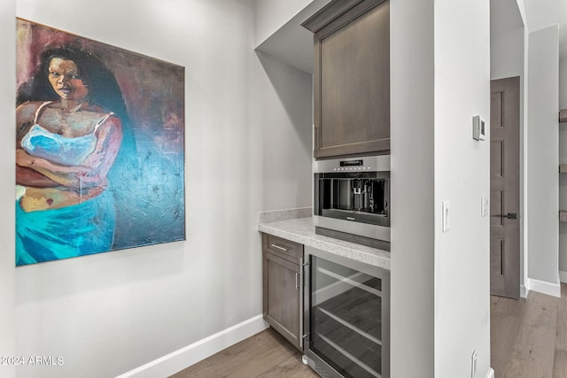 kitchen featuring wine cooler, dark brown cabinets, and light hardwood / wood-style flooring