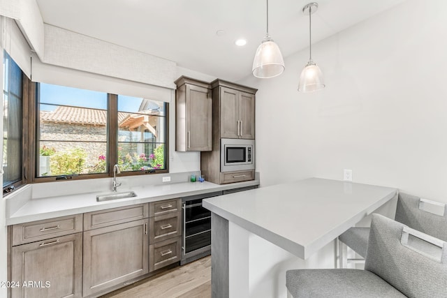 kitchen featuring a kitchen bar, stainless steel microwave, sink, light wood-type flooring, and wine cooler