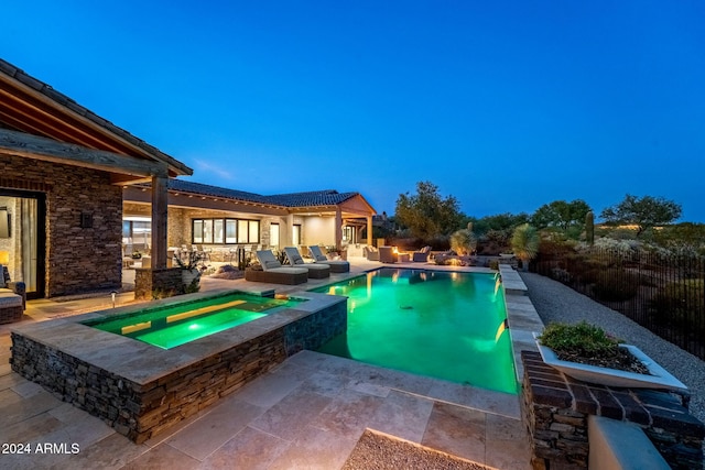 pool at dusk with an in ground hot tub and a patio area