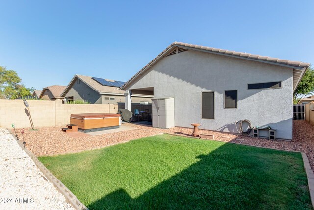 rear view of house featuring a hot tub, a lawn, a fenced backyard, and stucco siding