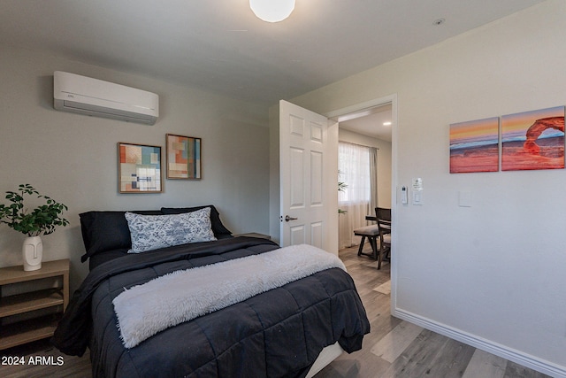 bedroom with baseboards, a wall unit AC, and wood finished floors