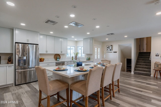 kitchen with appliances with stainless steel finishes, white cabinetry, a kitchen island, a breakfast bar area, and light hardwood / wood-style flooring