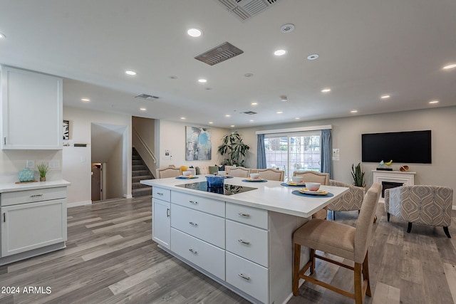 kitchen with white cabinets, a breakfast bar, light hardwood / wood-style flooring, a center island, and black electric stovetop