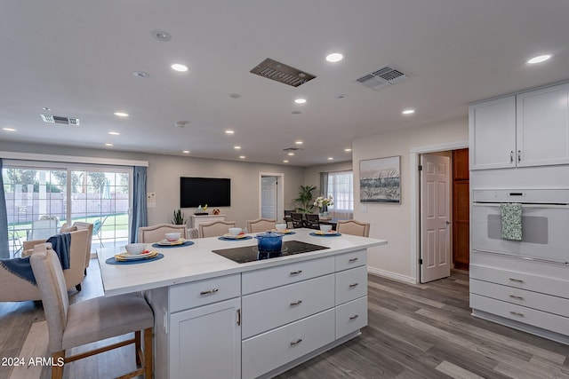 kitchen featuring a breakfast bar, white cabinets, oven, hardwood / wood-style floors, and black electric cooktop