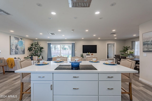 kitchen with white cabinets, black electric stovetop, light hardwood / wood-style floors, and a kitchen island