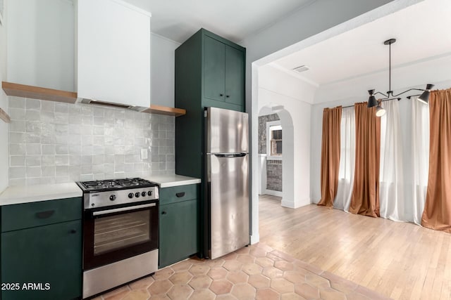 kitchen with green cabinetry, hanging light fixtures, appliances with stainless steel finishes, light hardwood / wood-style floors, and decorative backsplash