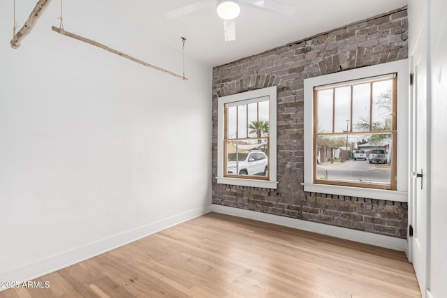 unfurnished room featuring light hardwood / wood-style flooring, ceiling fan, and brick wall