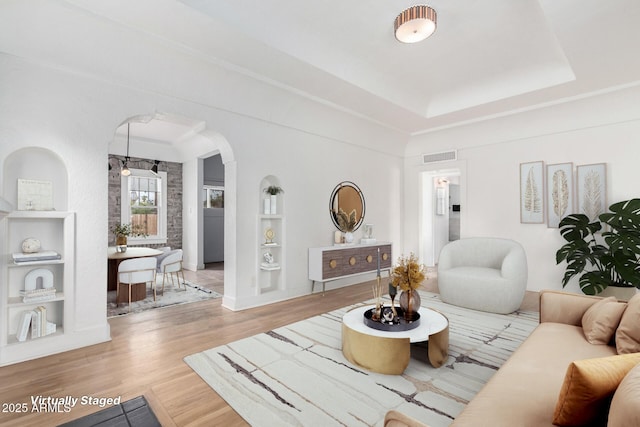 living room with a tray ceiling, wood-type flooring, and built in features