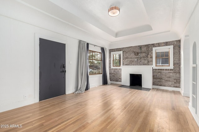 unfurnished living room with brick wall, a raised ceiling, and light hardwood / wood-style floors