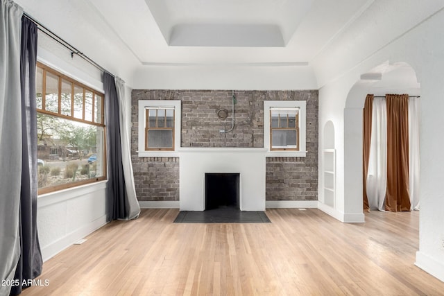 unfurnished living room featuring a raised ceiling, light hardwood / wood-style flooring, and brick wall