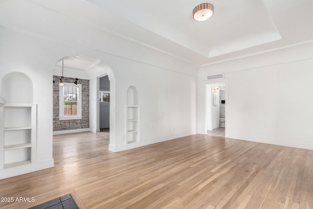 unfurnished living room featuring a tray ceiling, built in shelves, and light hardwood / wood-style flooring