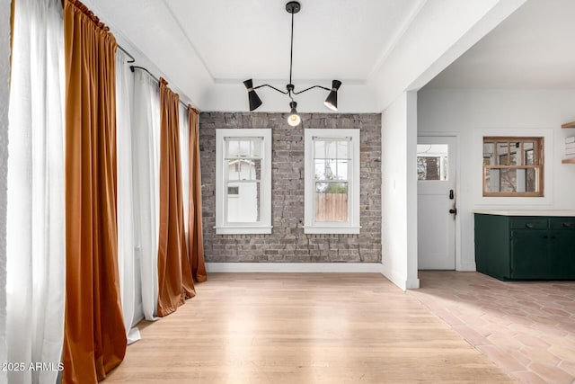 unfurnished dining area featuring a raised ceiling and light hardwood / wood-style floors