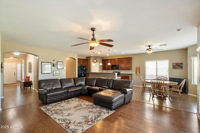 living area featuring arched walkways, a ceiling fan, baseboards, visible vents, and dark wood-style floors