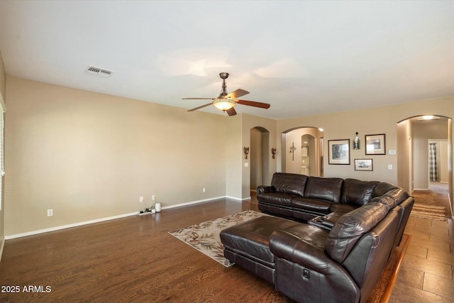 living room featuring arched walkways, a ceiling fan, baseboards, wood finished floors, and visible vents