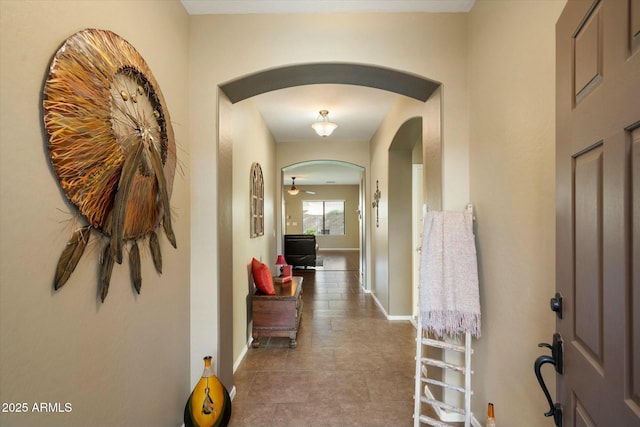 corridor featuring baseboards, arched walkways, and tile patterned flooring