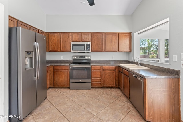 kitchen with brown cabinets, appliances with stainless steel finishes, a sink, and dark countertops