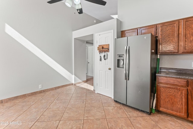 kitchen with stainless steel fridge with ice dispenser, light tile patterned floors, dark countertops, ceiling fan, and high vaulted ceiling