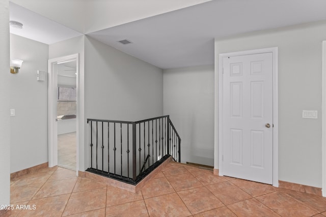 interior space with visible vents, baseboards, an upstairs landing, and light tile patterned flooring