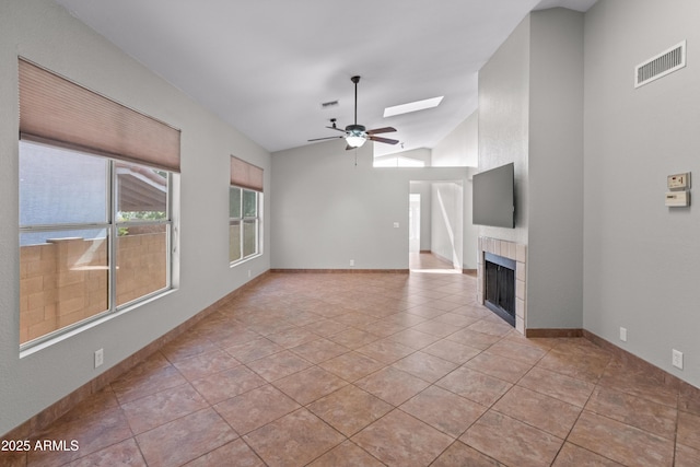 unfurnished living room with a tiled fireplace, visible vents, a ceiling fan, and lofted ceiling with skylight