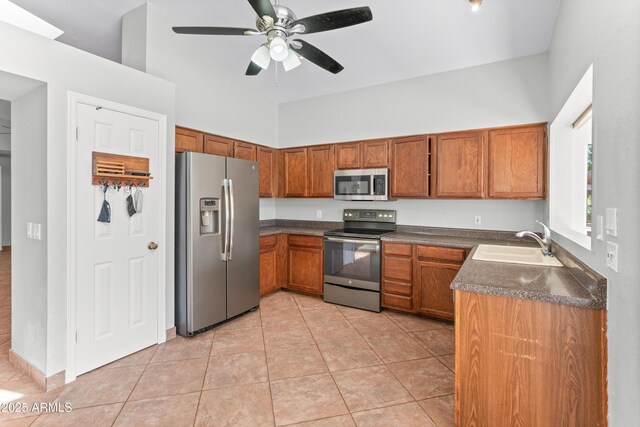 kitchen with high vaulted ceiling, dark countertops, a sink, stainless steel appliances, and brown cabinets