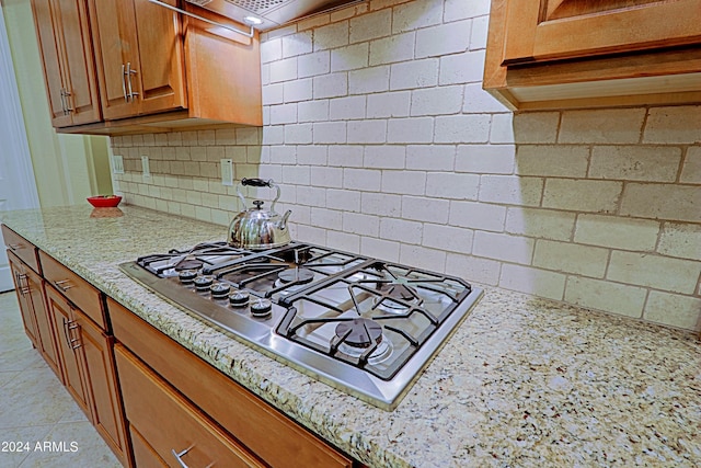 kitchen featuring backsplash, brown cabinets, light stone countertops, and stainless steel gas stovetop