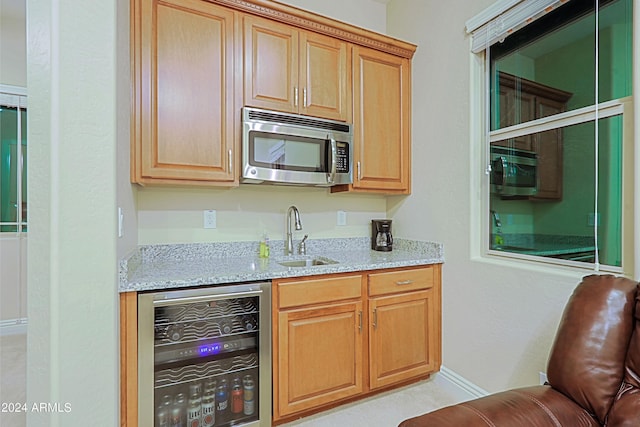 kitchen with light stone counters, stainless steel microwave, beverage cooler, and a sink