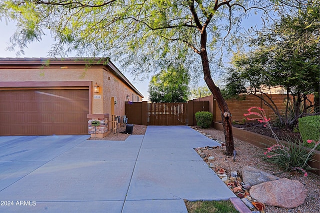 view of side of property featuring stucco siding, driveway, fence, and a gate