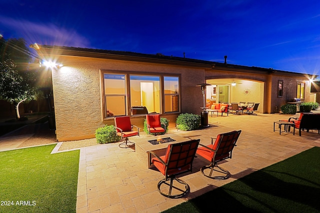 back of house at night with a patio area, stucco siding, and an outdoor fire pit