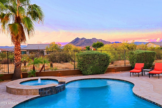 view of pool featuring a patio, fence, a mountain view, and a pool with connected hot tub