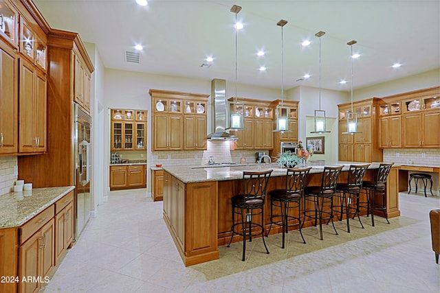 kitchen with wall chimney exhaust hood, brown cabinetry, visible vents, and a spacious island