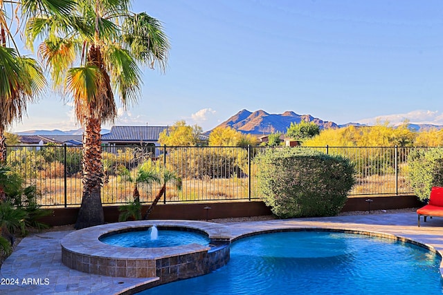 view of swimming pool featuring fence, a mountain view, and a pool with connected hot tub