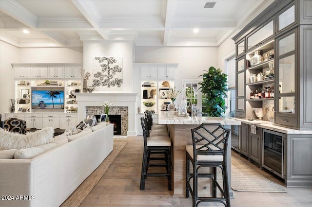 kitchen with a kitchen breakfast bar, beverage cooler, beam ceiling, a fireplace, and gray cabinets