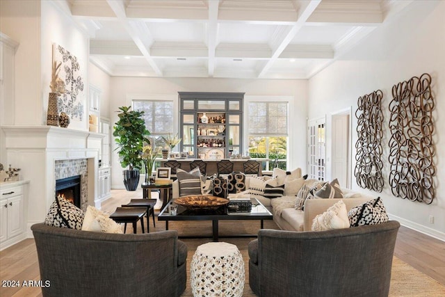 living room featuring coffered ceiling, beamed ceiling, light hardwood / wood-style floors, a tiled fireplace, and ornamental molding