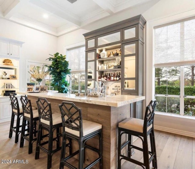 bar with white cabinets, beam ceiling, light hardwood / wood-style floors, and coffered ceiling