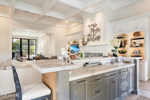 kitchen featuring a breakfast bar area, beamed ceiling, white cabinets, and coffered ceiling