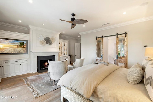 bedroom with a barn door, crown molding, light hardwood / wood-style flooring, and ceiling fan