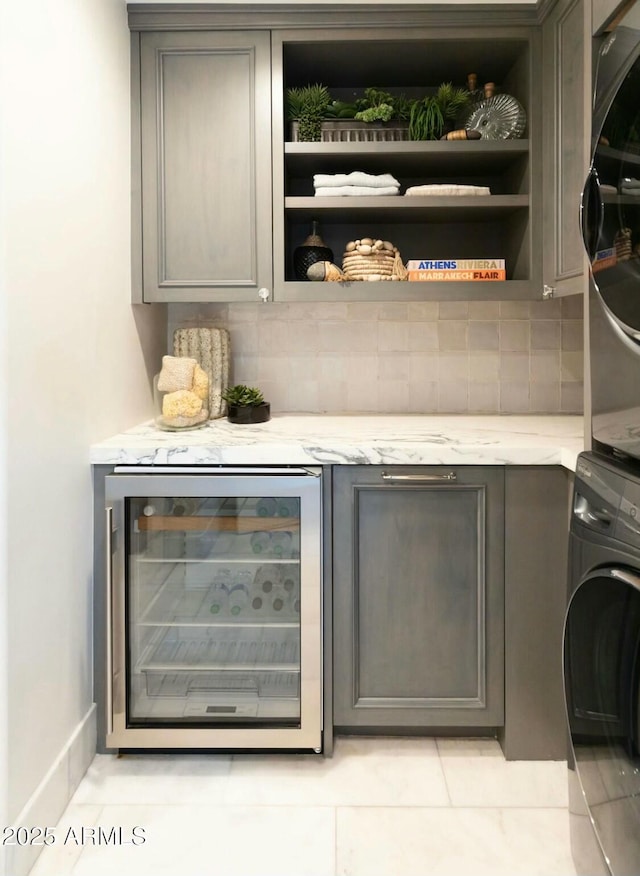 bar featuring backsplash, wine cooler, gray cabinets, and stacked washer and clothes dryer