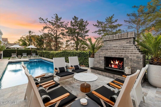 pool at dusk with an outdoor brick fireplace and a patio area