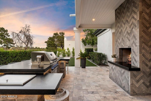 patio terrace at dusk featuring a tiled fireplace and area for grilling