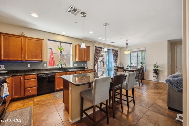 kitchen featuring dark stone counters, a kitchen island, a kitchen breakfast bar, dishwasher, and hanging light fixtures