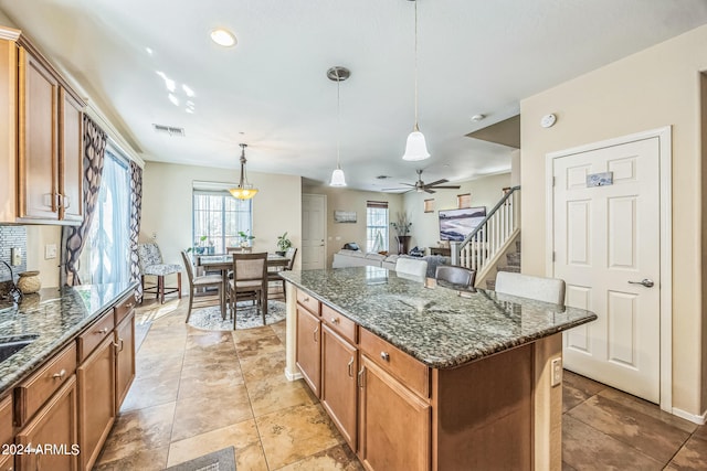 kitchen featuring pendant lighting, dark stone countertops, ceiling fan, and a center island