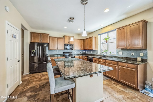 kitchen with a breakfast bar, decorative light fixtures, sink, black appliances, and a center island