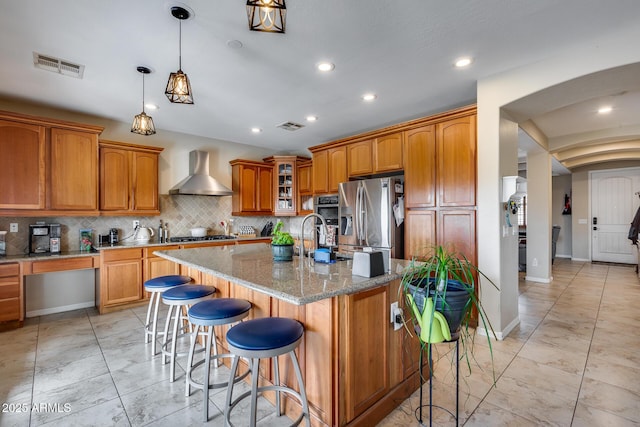 kitchen with brown cabinetry, visible vents, appliances with stainless steel finishes, and wall chimney range hood